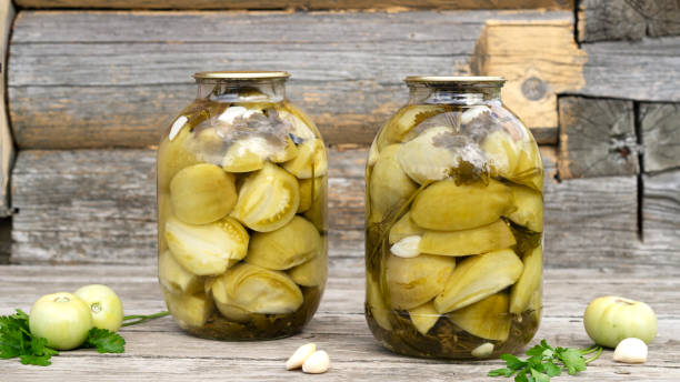 decorative homemade pickled green tomatoes for winter in a glass jars with garlic and parsley. - pickled green tomatoes stock pictures, royalty-free photos & images