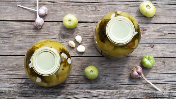 decorative homemade pickled green tomatoes for winter in a glass jars with garlic and parsley. home conservation. top view. - pickled green tomatoes stock pictures, royalty-free photos & images